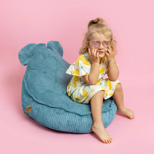 Child sitting on a blue bean bag chair against a pink background